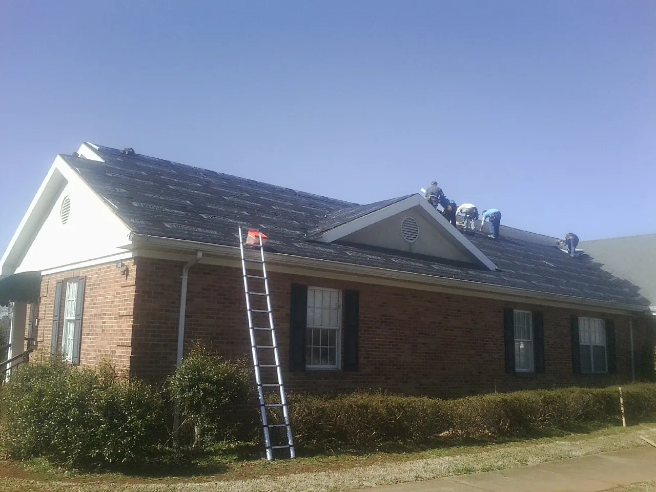 Crew tearing shingles off a brick ranch roof with a ladder set — Metal Roof Repair work by our crew in Prairie City