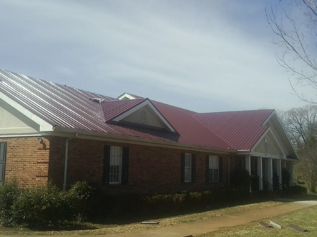 Red metal roof with gabled entries on a long brick building, from a Hail Damage Roof Repair job in Prairie City
