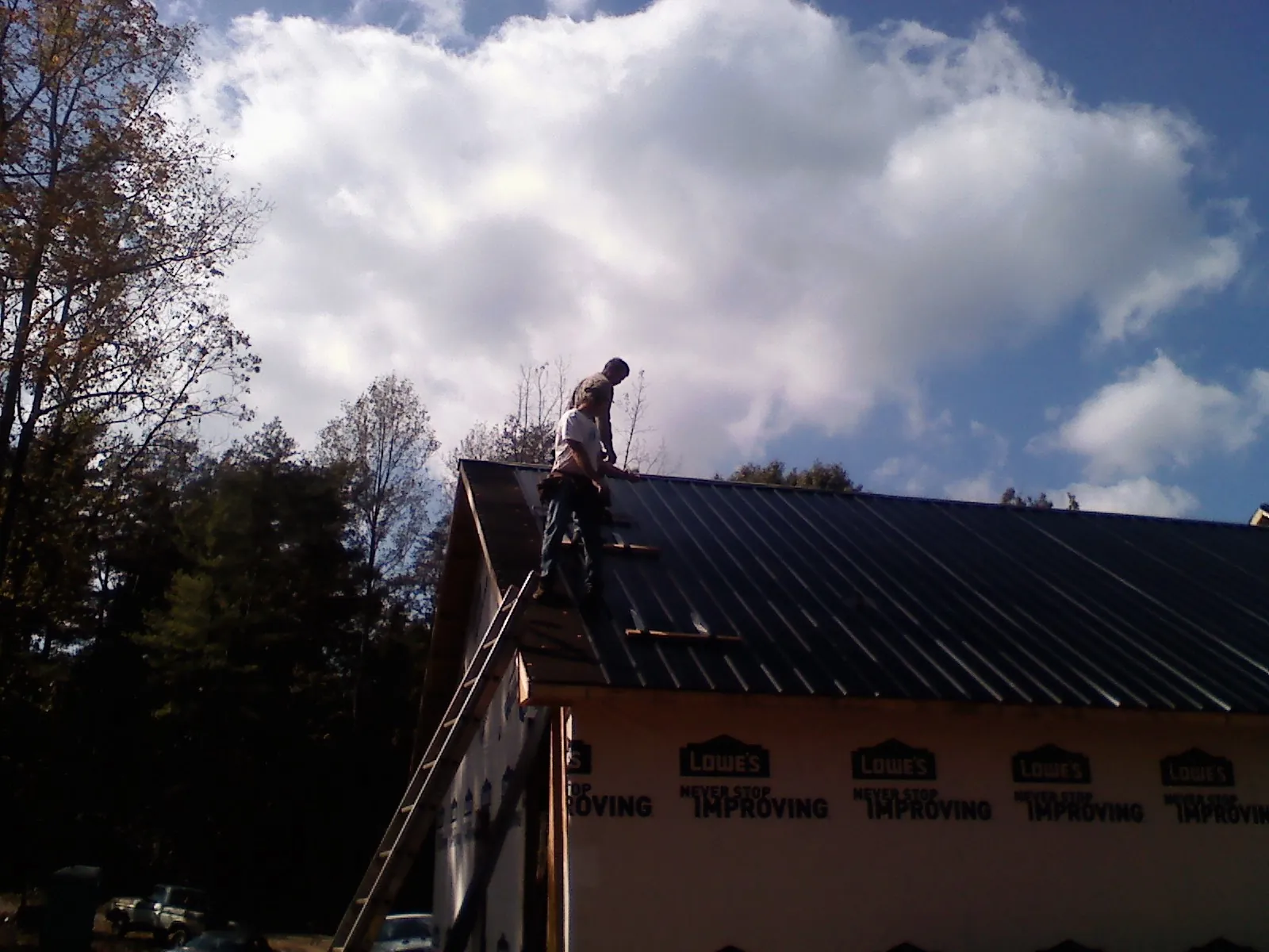 Roofer fastening dark metal panels high against a cloudy sky, from a Roof Inspection job in Prairie City