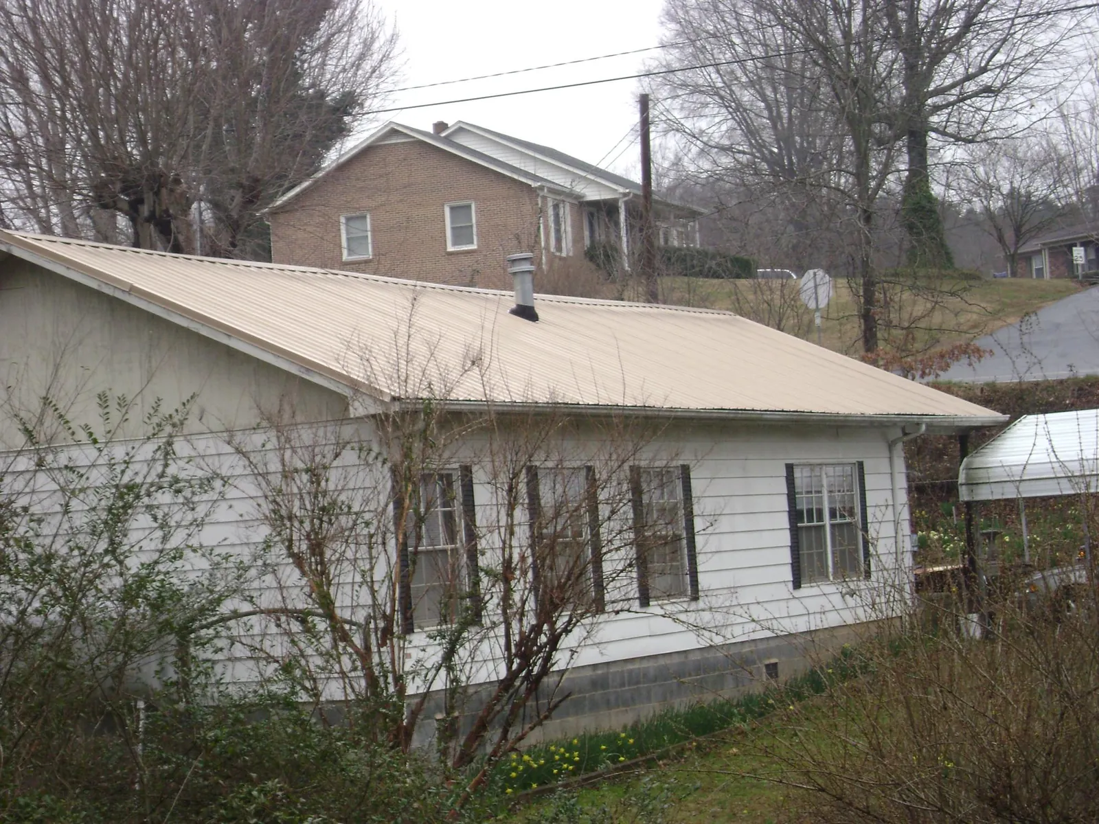 Tan metal roof on a white sided house set into a hillside — Commercial Roofing by Roofing Brothers in Prairie City